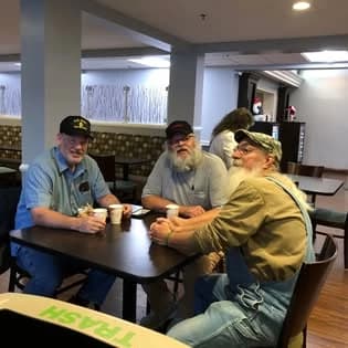 Three men in caps talking over coffee at a table